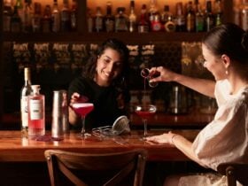 lady pouring a cocktail in the glass while another lady garnishes a drink at the bar table