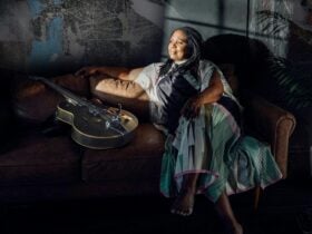 Ruthie Foster posing with her guitar on a couch