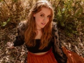 A young woman with red hair sitting on the ground looking up at the camera
