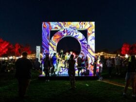 People gather around a glowing, colourful art installation at a night festival.