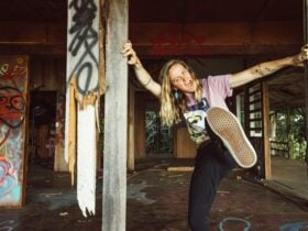 Tessa Devine leaning around a graffiti-covered pillar in an abandoned building, one leg raised.