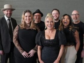 Group of smiling performers from The Adele Show posing together, dressed in black .