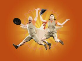A man and lady jumping in the air, holding hats, surprised looks on their faces with a chicken.