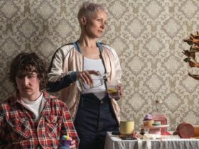 Two characters from the play against wallaper, one sitting, one standing both looking opposite ways.