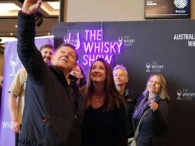 A group of attendees gather in front of a Whisky Show banner and neon sign for a selfie.