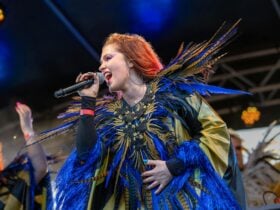 A woman wearing a unique costumer with feathers, singing on stage with a microphone to her mouth.