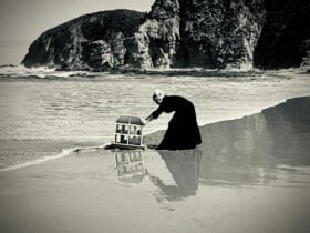 Woman in a black dress dragging a miniature house our of the ocean