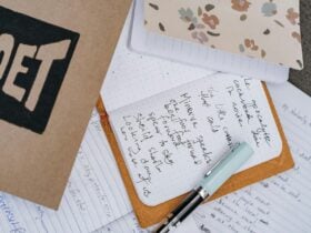 Several notebooks, one in the centre laying open to reveal a handwritten poem, and a light blue pen