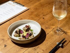 handmade ceramic bowl with seared kingfish pieces inside, a glass of white wine, a menu on table