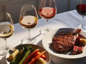 Steak, vegetables and four glasses of wine on top of a white table