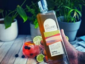 A bottle of liqueur being held with a cocktail in the background
