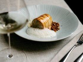a cylindrical food with white foam and crumble in a blue plate with cutlery and a wine glass