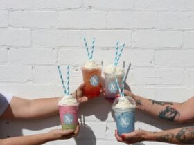 four colourful beverages being held against a white wall