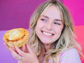 A person smiling and holding a delicious pie in front of a vibrant pink background