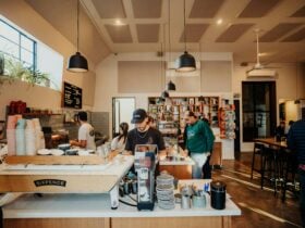 Man making coffee in black t-shirt and black cap at white branded coffee machine in open room