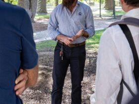 Tour guide speaking to two visitors in the Town Hall Gardens. Large tree trunks in the background.