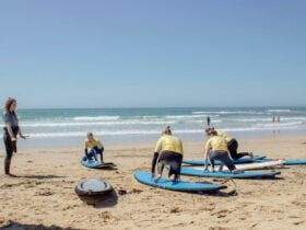 Four surfers practicing standing on boards on the sand with the surf instructor providing direction.