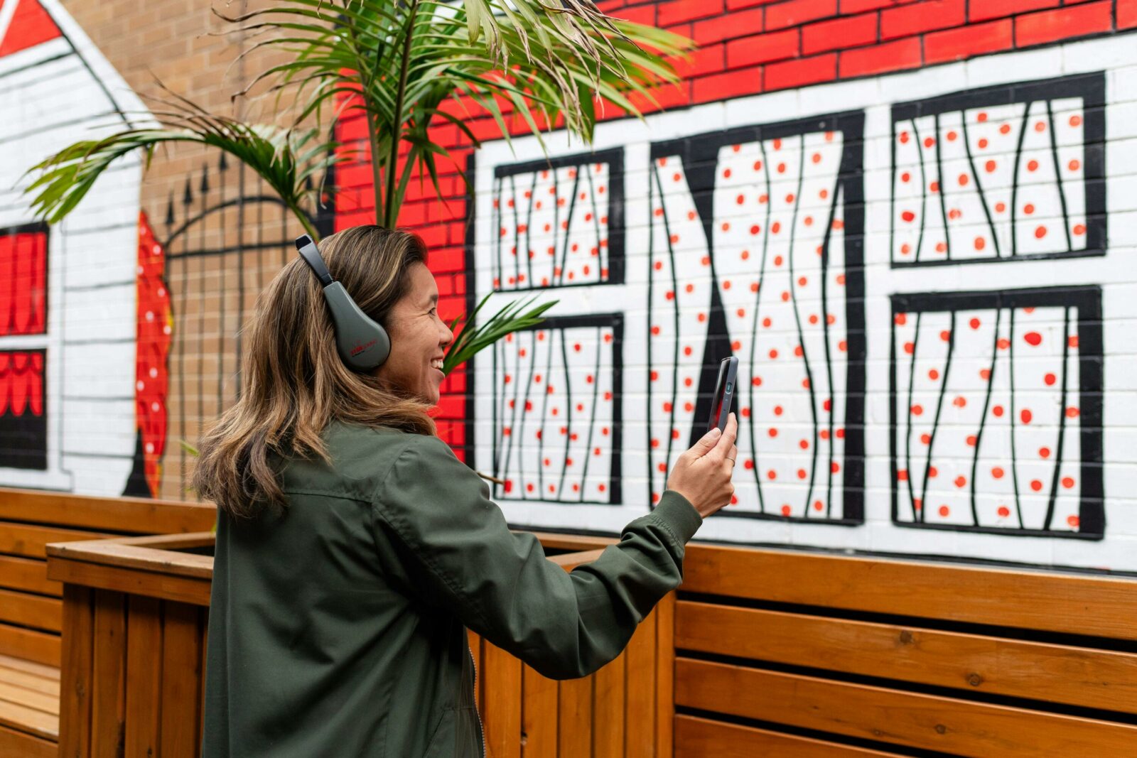 adult wearing headphones and holding out phone in front of street art