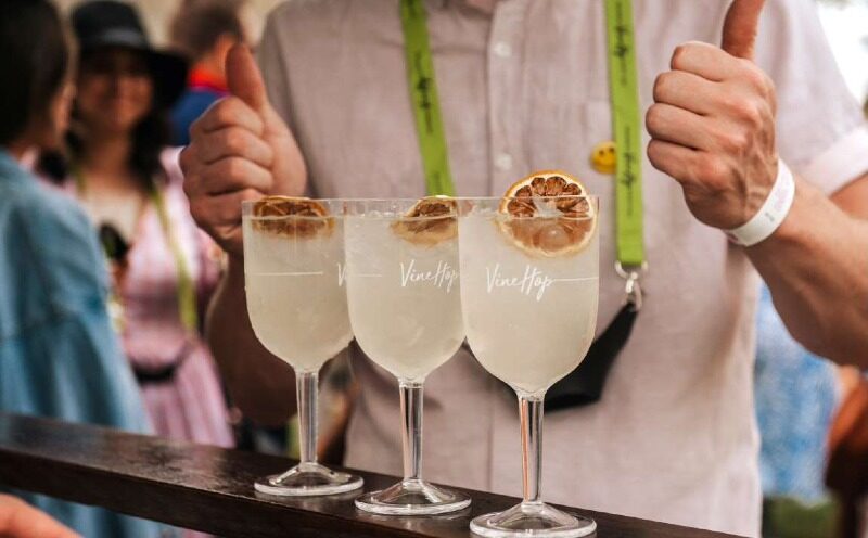Three drinks lined up on the bar with VineHop written on the glass and the customer giving thumbs up in the background
