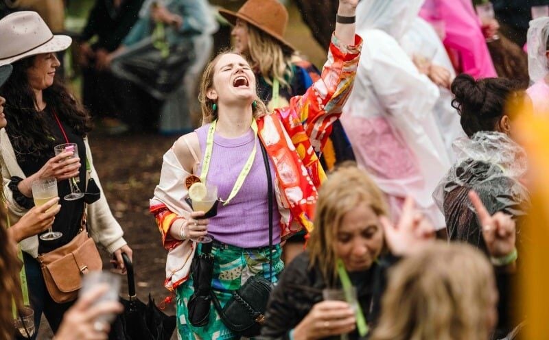 Woman dancing in the rain with her hands up in the air and VineHop glass in her hand, head thrown back, eyes closed, loving the moment
