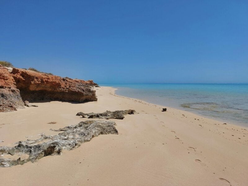 Red rock leading down to the sand and water.