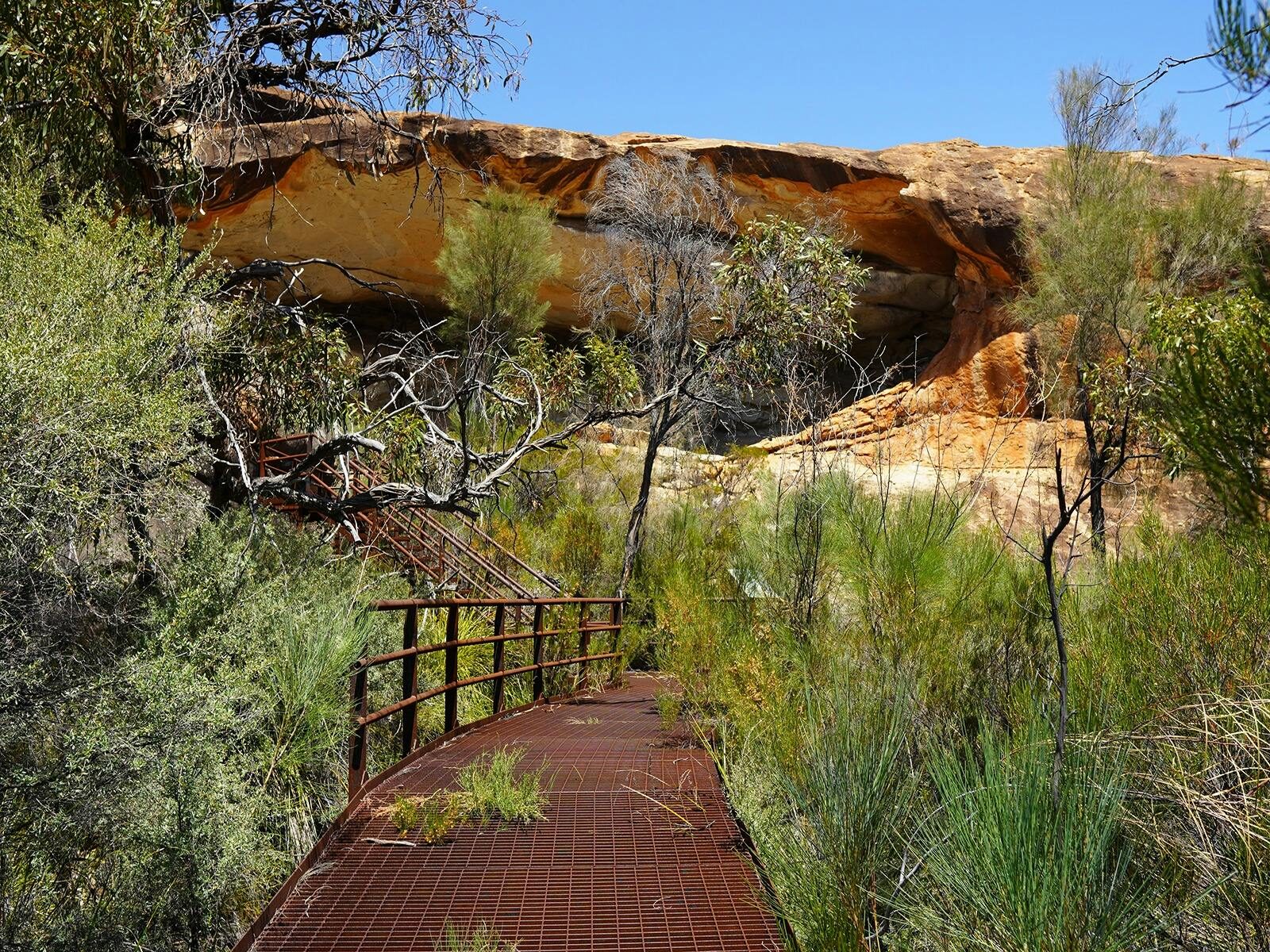 Metal boardwalk near rock overhang.