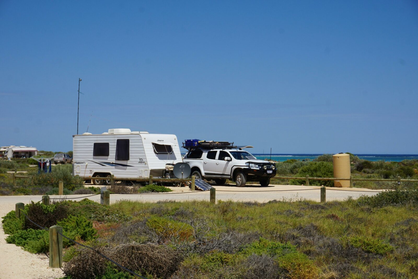 Four wheel drive parked next to a caravan in a space surrounded by small shrubs.