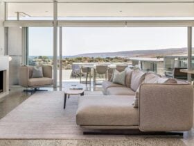 Lounge room in grey tones in foreground with view over ocean and cape in background.