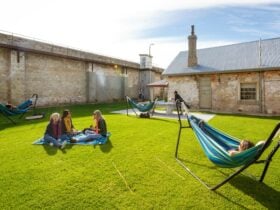Guests sitting on the grass and lying in a hammock in outdoor area of YHA Fremantle Prison