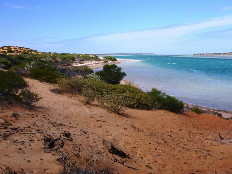 Red sandy bay with clear blue water.