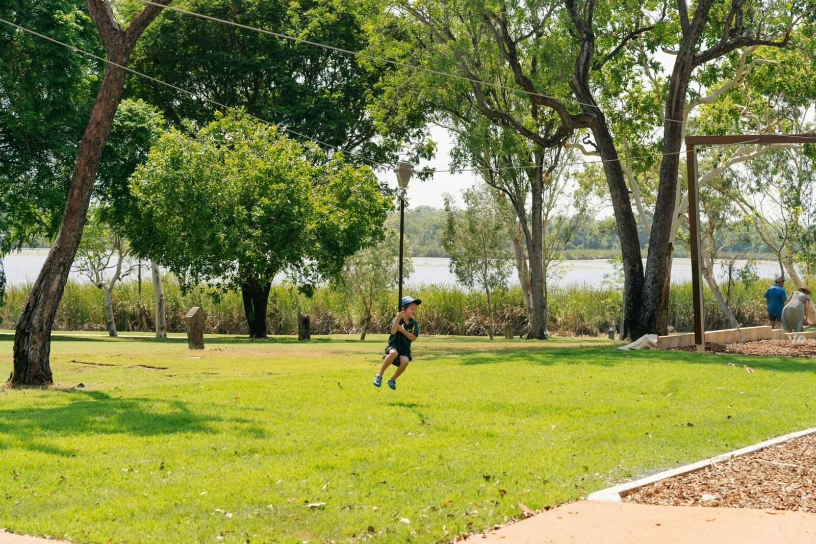 a child plays on a flying fox over a grassed area, with trees and Lake Kununurra in the background