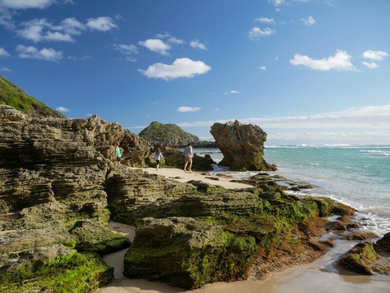 People walking near rocks on the edge of the river.