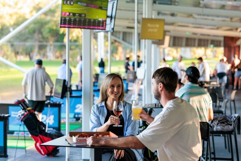 A couple enjoying a drink while they practice their golf at the driving range