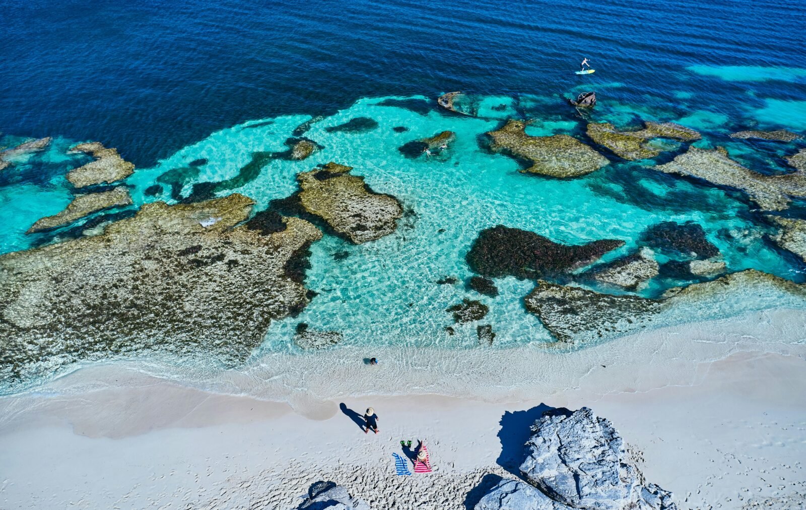 Aerial view of reef and clear blue water on a beach.