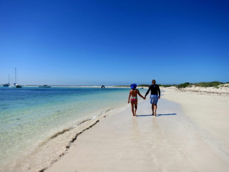 Two people walking on the beach holding hands.