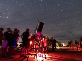 People lined up at big telescope, to look through.