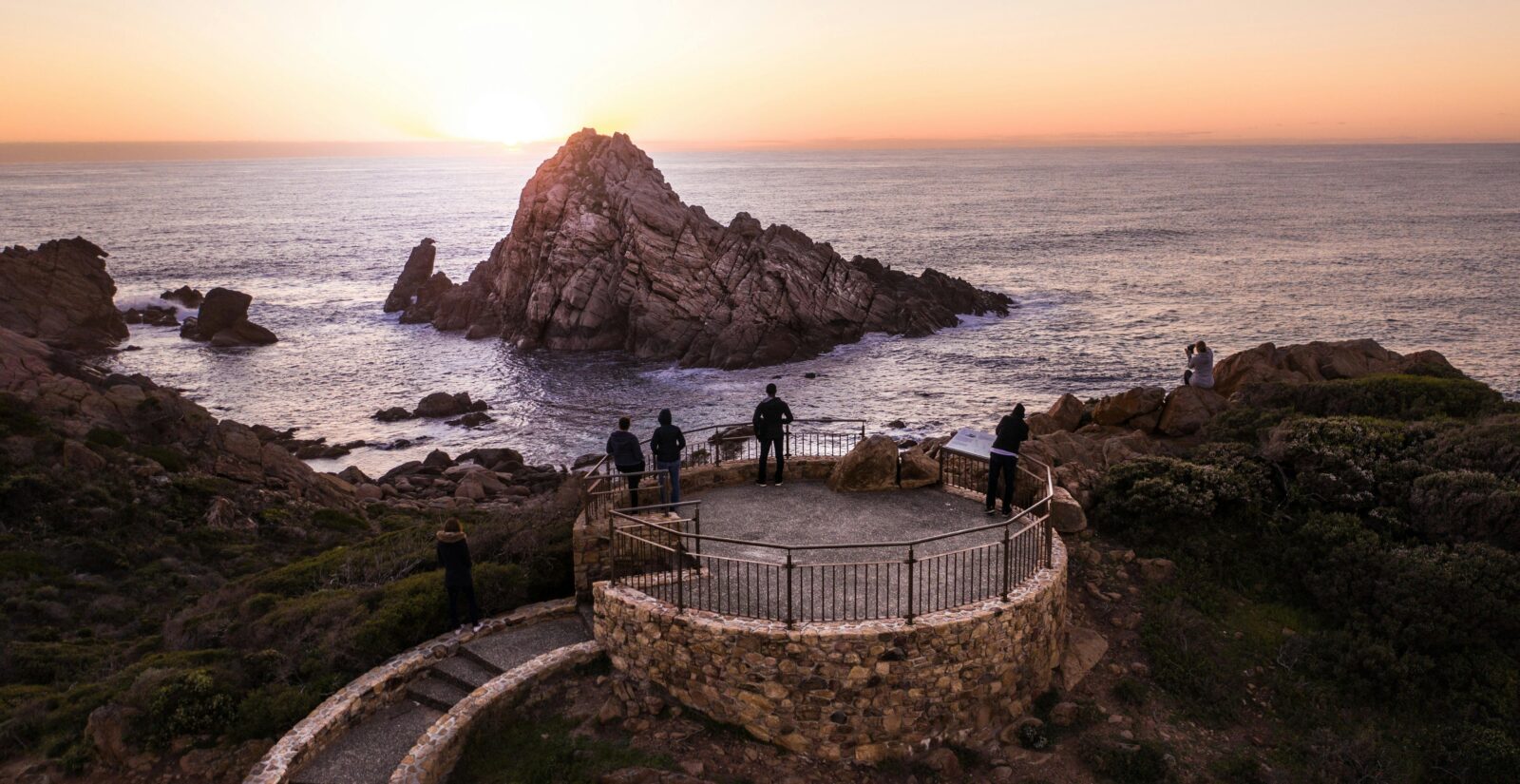 People standing on a lookout overlooking the ocean and a large granite rock/small island.