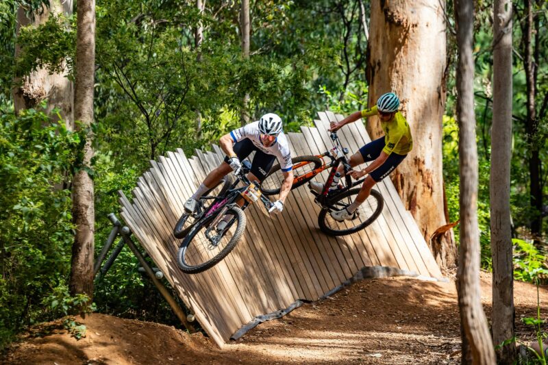 Two male MTB riders, riding along a horizontal path.