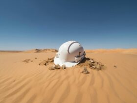 A white construction helmet lying on the ground, red dirt below and blue sky above.