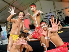 Five performers with body paint pose on stage with hands raised during a cultural dance.