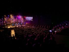 Packed theatre with a full audience watching a colorful live concert on a brightly lit stage now!!!!