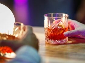 Close-up photograph of two glasses filled with red liquid being held at a table.