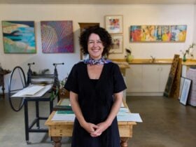 Smiling lady in black standing in front of colourful art and a printing press