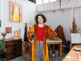 Young woman in bright zany clothing posing for the camera surrounded by paintings