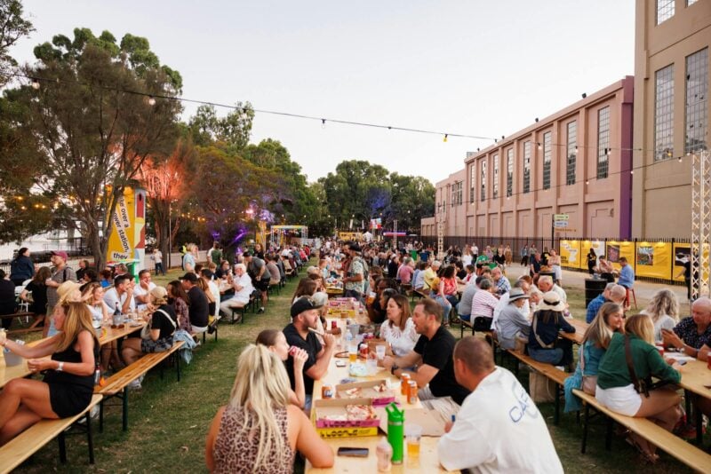 Festival-goers eat and drink on shared benches at Casa Musica, enjoying the atmosphere