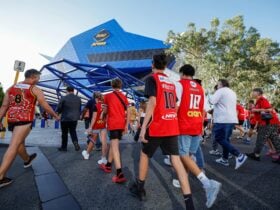 Perth Wildcats fans wearing red merchandise walk into RAC Arena under a clear blue Perth sky