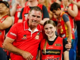 A dad and daughter smile and face the camera in the crowd of a Wildcats game wearing red merchandise
