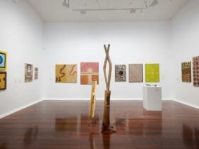 Numerous artworks on display in a gallery including two wooden installations in the centre.