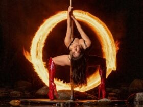 long hair Asian woman red knee high stiletto boots back bend on pole surrounded by ring of fire