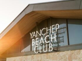 A modern building facade with large windows and a slanted roof, featuring a glowing sign that reads